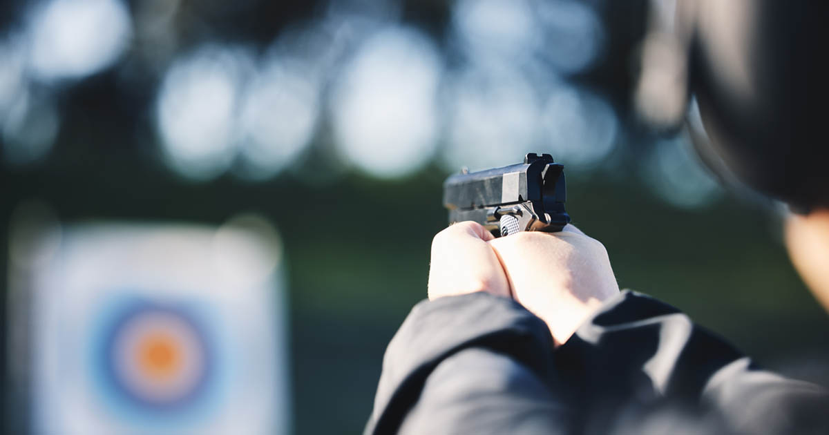 Person pointing a handgun at a target on an outdoor shooting range,
